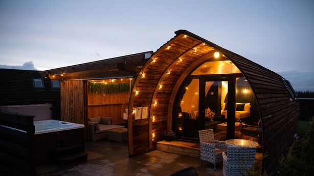 Una cabaña de madera con hidromasaje, mobiliario exterior y un porche cubierto.
