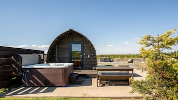 Een houten blokhut met een jacuzzi, een houten bank en een kleine tafel.