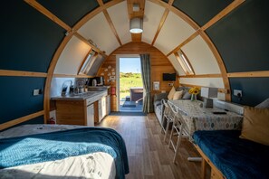 Une pièce accueillante, semi-ouverte, avec une voûte, un coin cuisine, un espace repas et deux lits.