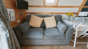 Una habitación acogedora con un sofá gris, un televisor montado en la pared y una mesita con un jarrón de girasoles.