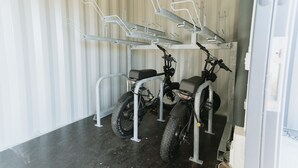 Una habitación con dos bicicletas eléctricas, un soporte de metal para bicicletas y una pared blanca con rayas verticales.