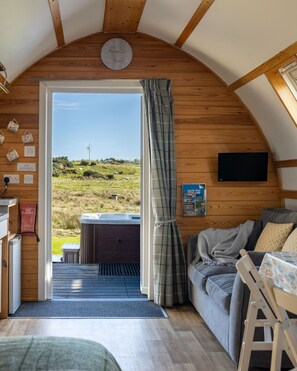 Ein gemütliches Zimmer mit Holzbalkendecke, einem Bett, einer Sitzecke mit Tisch und Blick auf ein grünes Feld.