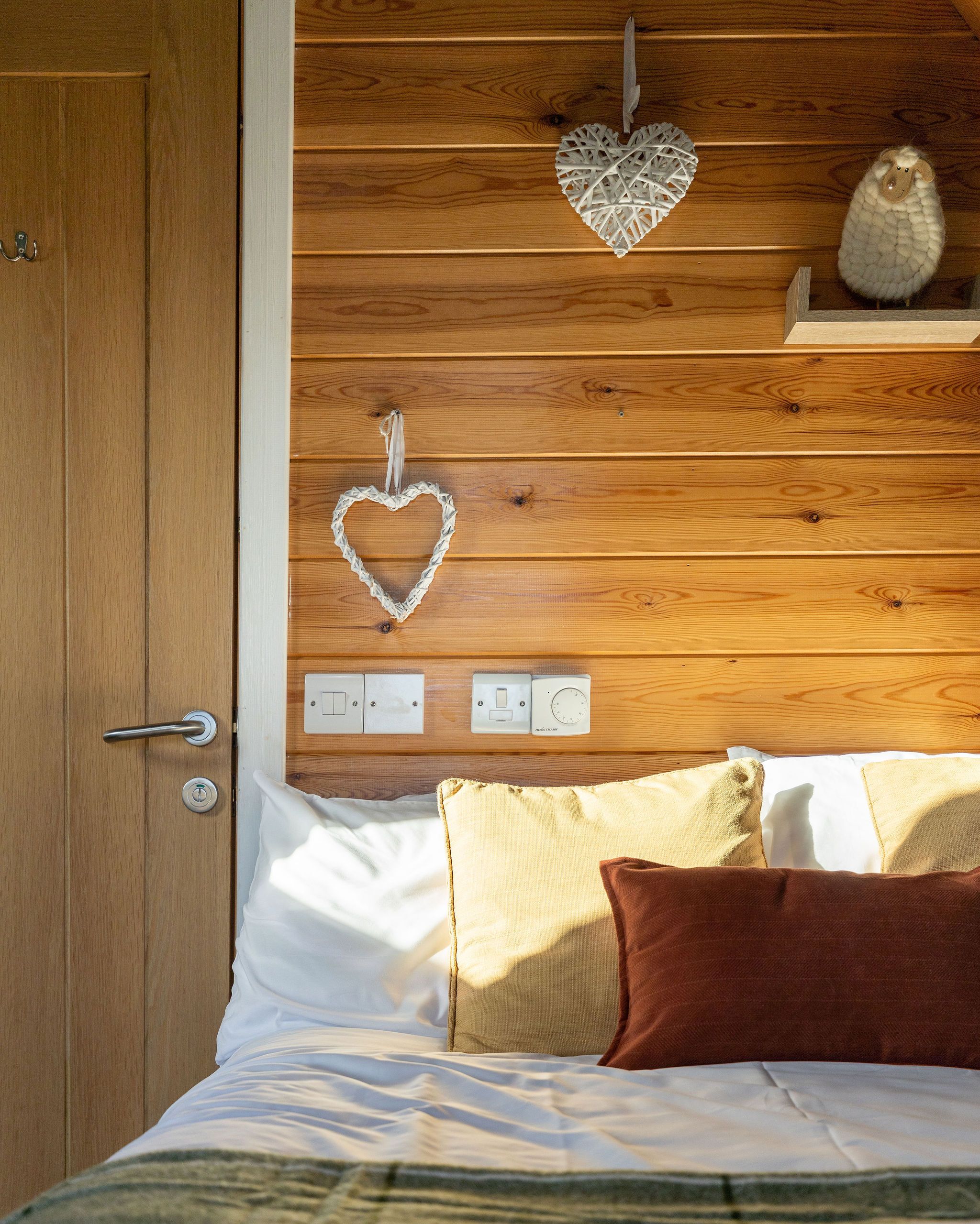 Ein Schlafzimmer mit einem hölzernen Kopfteil, zwei herzförmigen Dekorationen, einem Bett mit weißer und brauner Bettwäsche und einer kleinen Ablagefläche mit einem dekorativen Gegenstand.