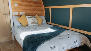 Una cama de madera con una colcha blanca y gris estampada, dos almohadas y una manta azul.