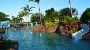 A pool area with lounge chairs, palm trees, and a water slide.