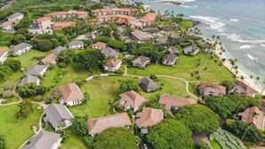 An aerial view of a coastal residential area with houses, green lawns, and a beach.