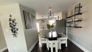Une cuisine moderne avec un plancher en bois foncé, des meubles blancs et un îlot central. Des luminaires suspendus sont placés au-dessus de l’îlot, et une horloge est accrochée au mur.