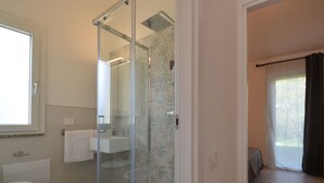 A modern bathroom with a glass-enclosed shower, a white sink, and a toilet.