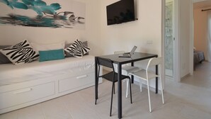 A modern living room with a white sofa, a flat-screen TV, and a laptop on a table.