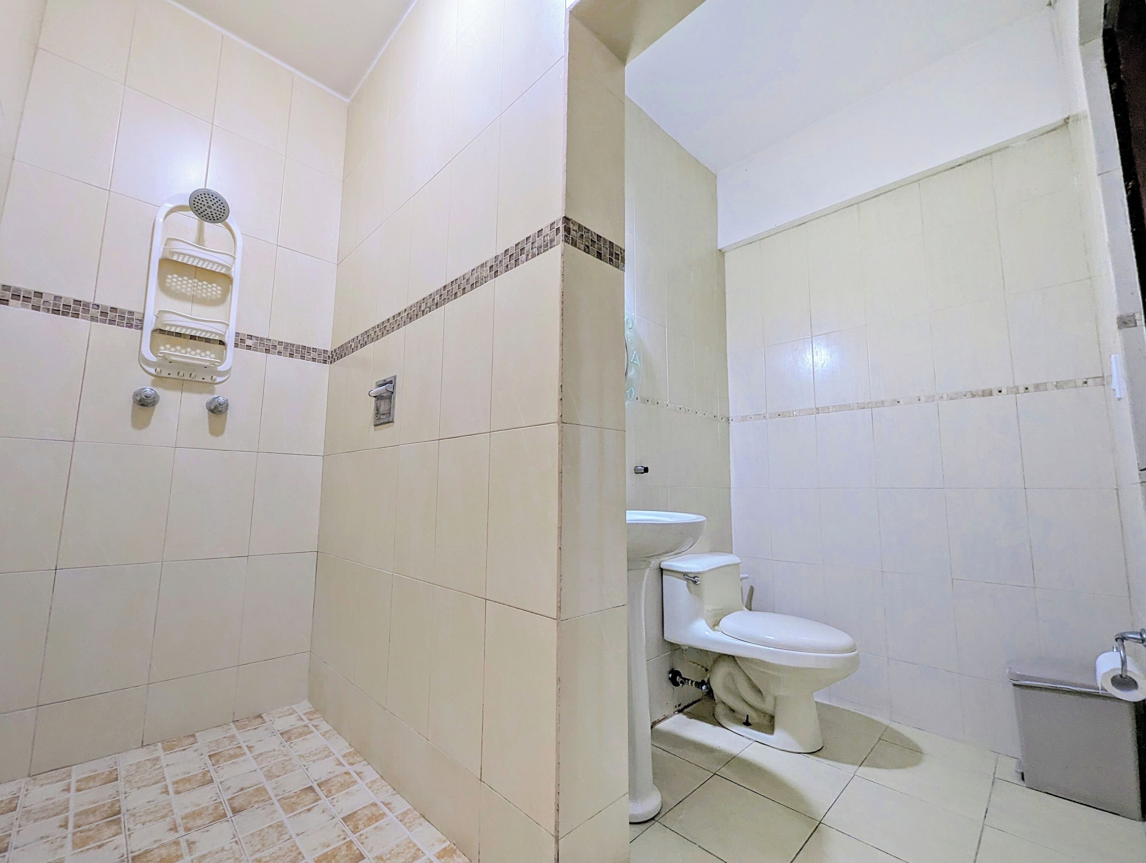 Une salle de bain comprenant des toilettes, un espace douche et un sol carrelé.