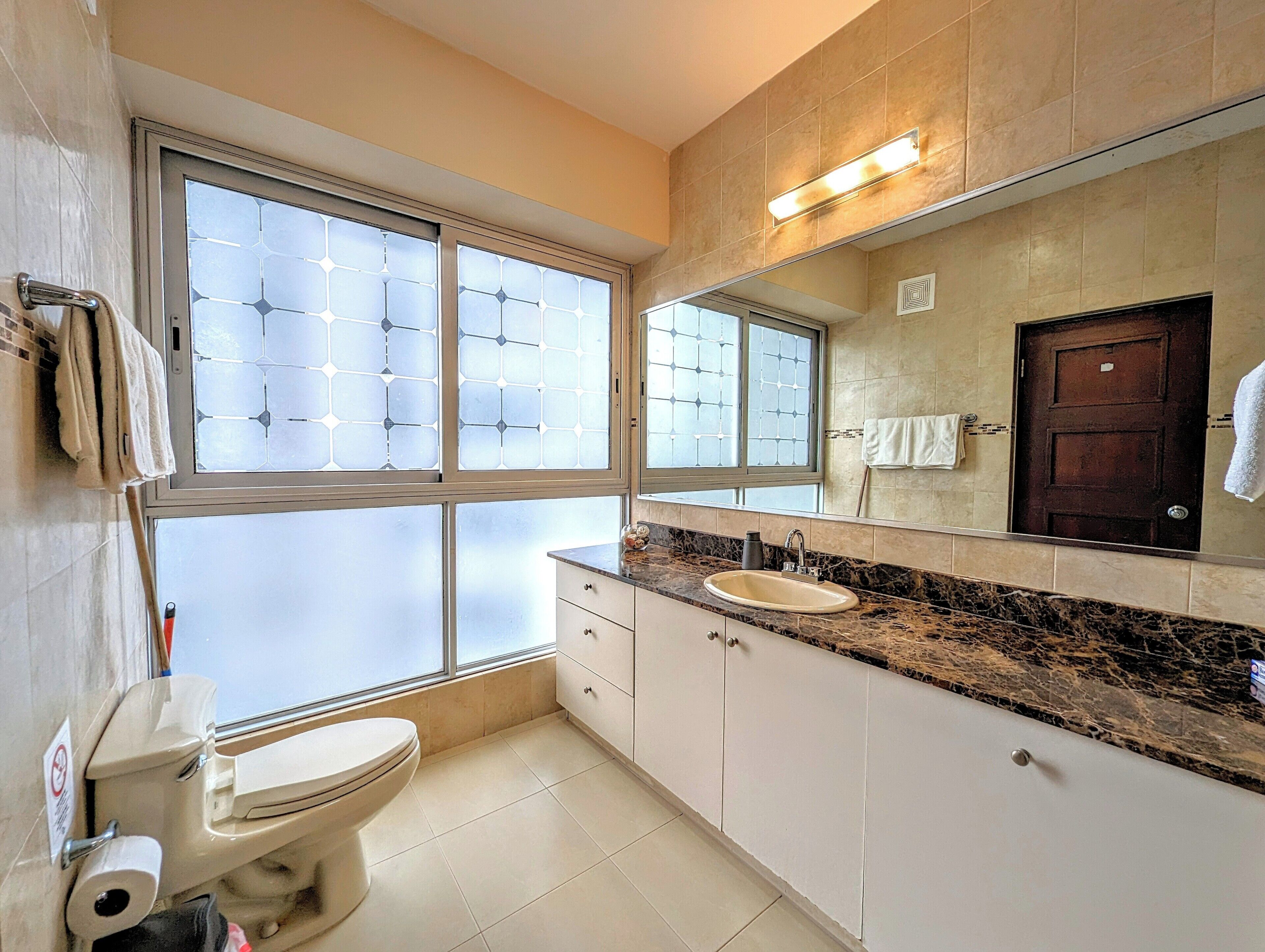 Un baño con inodoro, lavamanos y ventanas amplias.