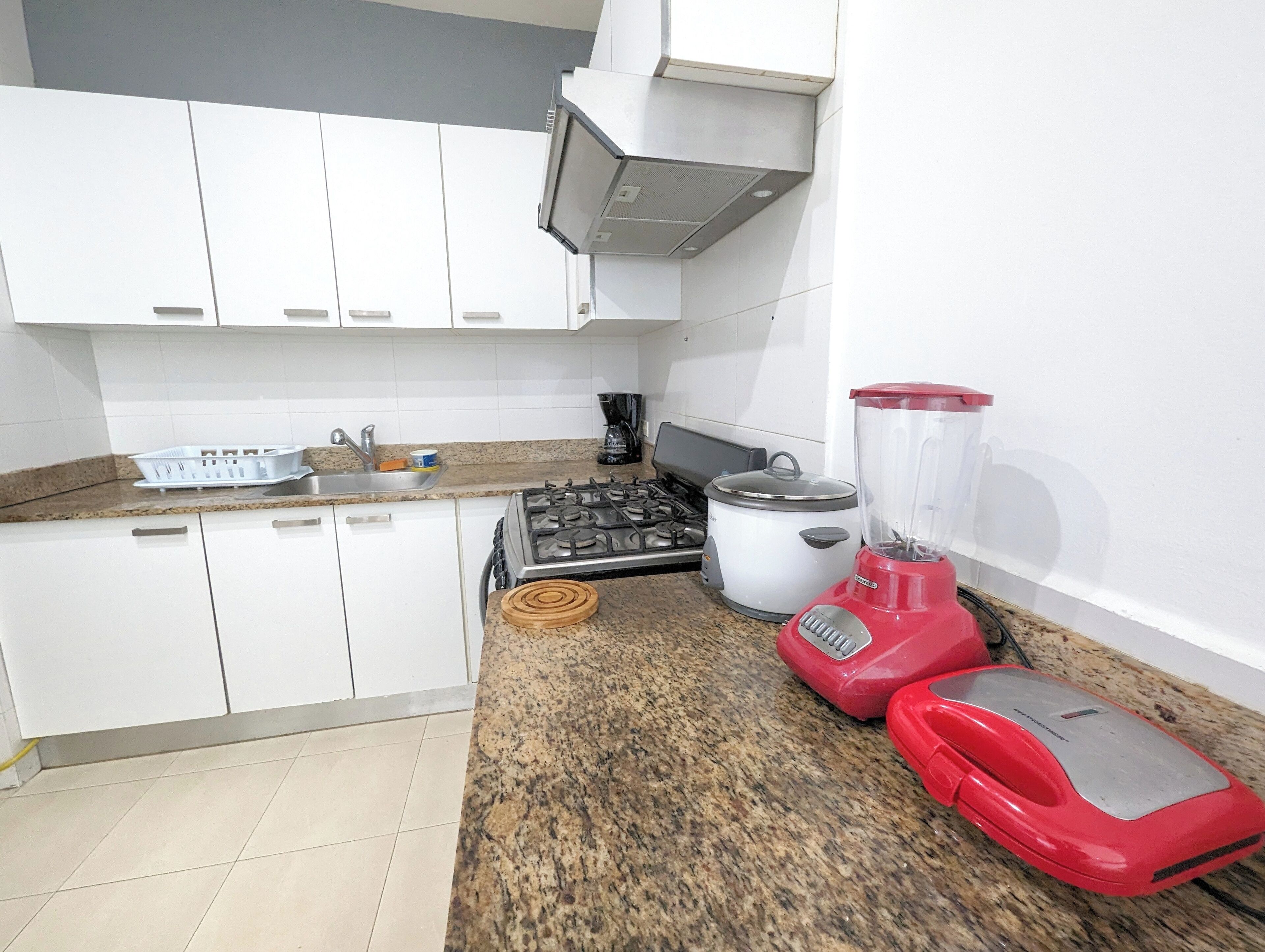 A kitchen with white cabinets, a granite countertop, a stove, a blender, and a coffee maker.