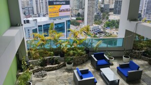 Un balcón interior moderno con vistas a la ciudad, amoblado con sofás azules y una mesita, rodeado de plantas en macetas.