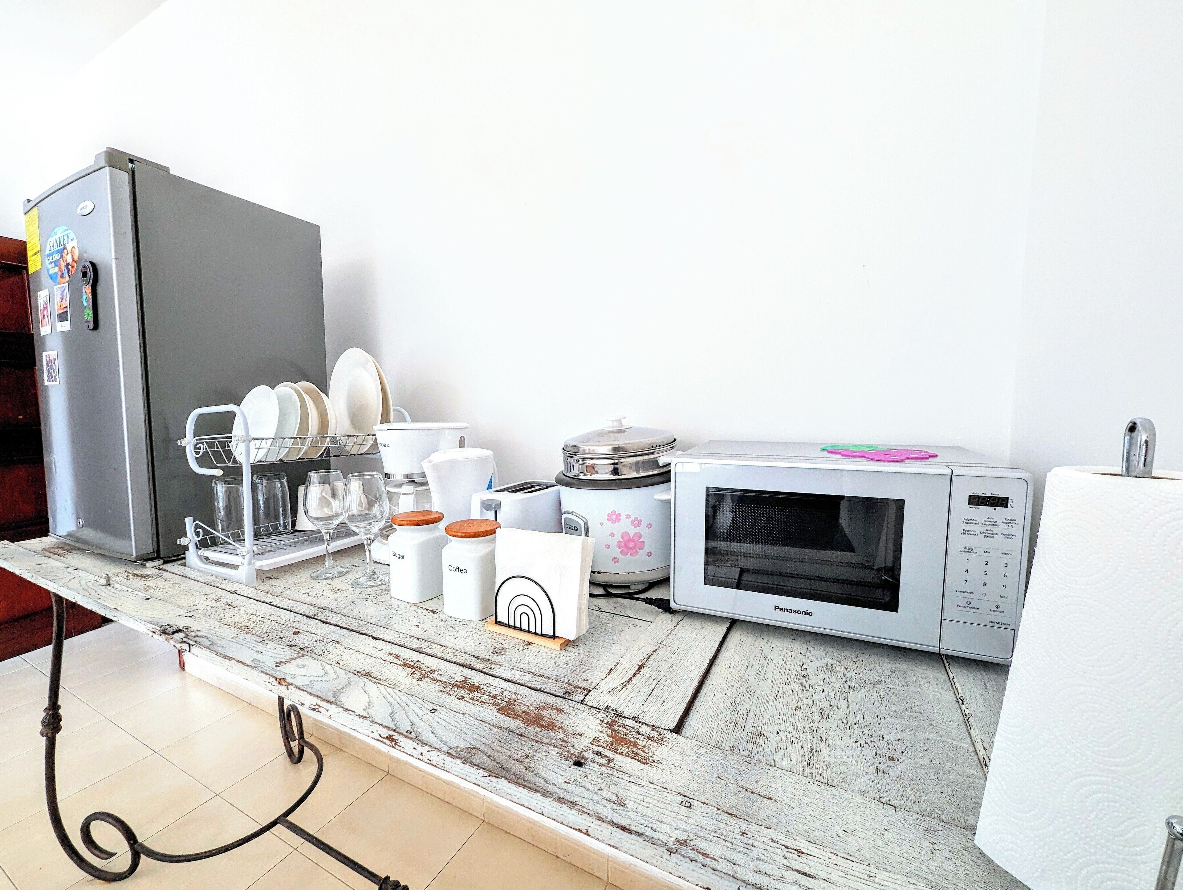 A kitchen with a refrigerator, microwave, and a dish rack with dishes and glasses.