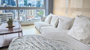 Un salón moderno con un ventanal grande, un sofá blanco, un plaid estampado y una pequeña mesa con una planta.