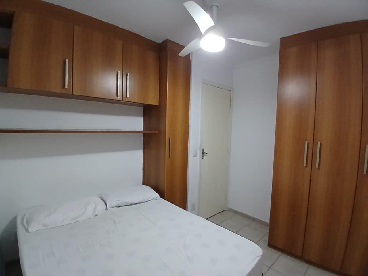 Un dormitorio con cama, armario de madera y ventilador de techo.
