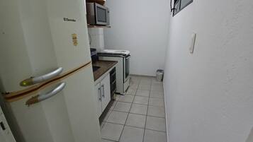 Een compacte keuken met een witte koelkast, een magnetron en een klein spoelbakje.