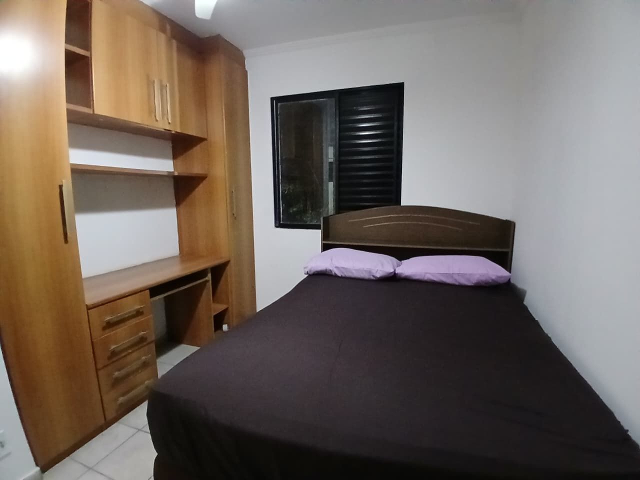 Un dormitorio con cama, un armario de madera y una ventana con persianas.