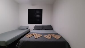 Un petit logement composé d’une seule pièce, comprenant un lit simple et un lit double, tous deux avec du linge de lit gris.