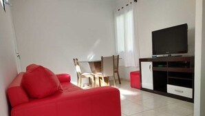 Un canapé rouge, une table à manger avec des chaises, un téléviseur posé sur un meuble et un buffet.