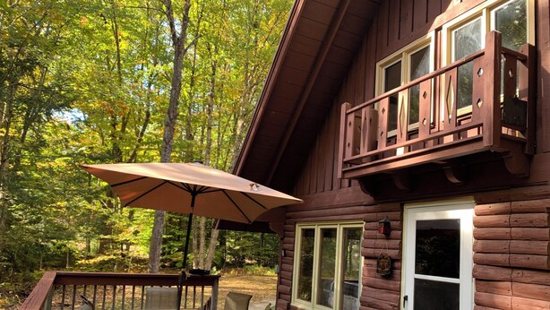 A wooden cabin with a deck, a table with chairs, and an umbrella.