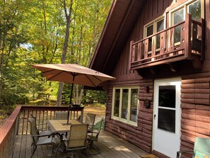 A wooden cabin with a deck, a table with chairs, and an umbrella.