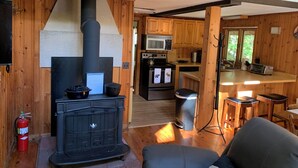 A cozy cabin interior with a wood-burning stove, a kitchen with a microwave, and a dining area with a table and chairs.