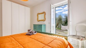 A bedroom with an orange bed, a green dresser, a white chair, and a window with a view of trees.
