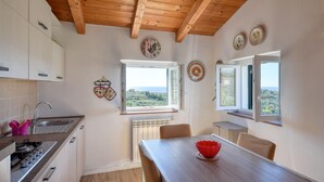 A kitchen with wooden beams, a view through the window, and a dining area with a table and chairs.