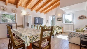 A cozy, well-lit room with wooden beams on the ceiling, a dining table with chairs, a television, and a bed with floral bedding.