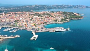 An aerial view of a coastal town with a marina, boats, and a lighthouse. - Camping Village Capo d'Orso by Interhome (Palau)