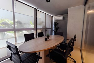 Uma sala de conferências com uma mesa redonda, cadeiras pretas e grandes janelas com vista para o verde.