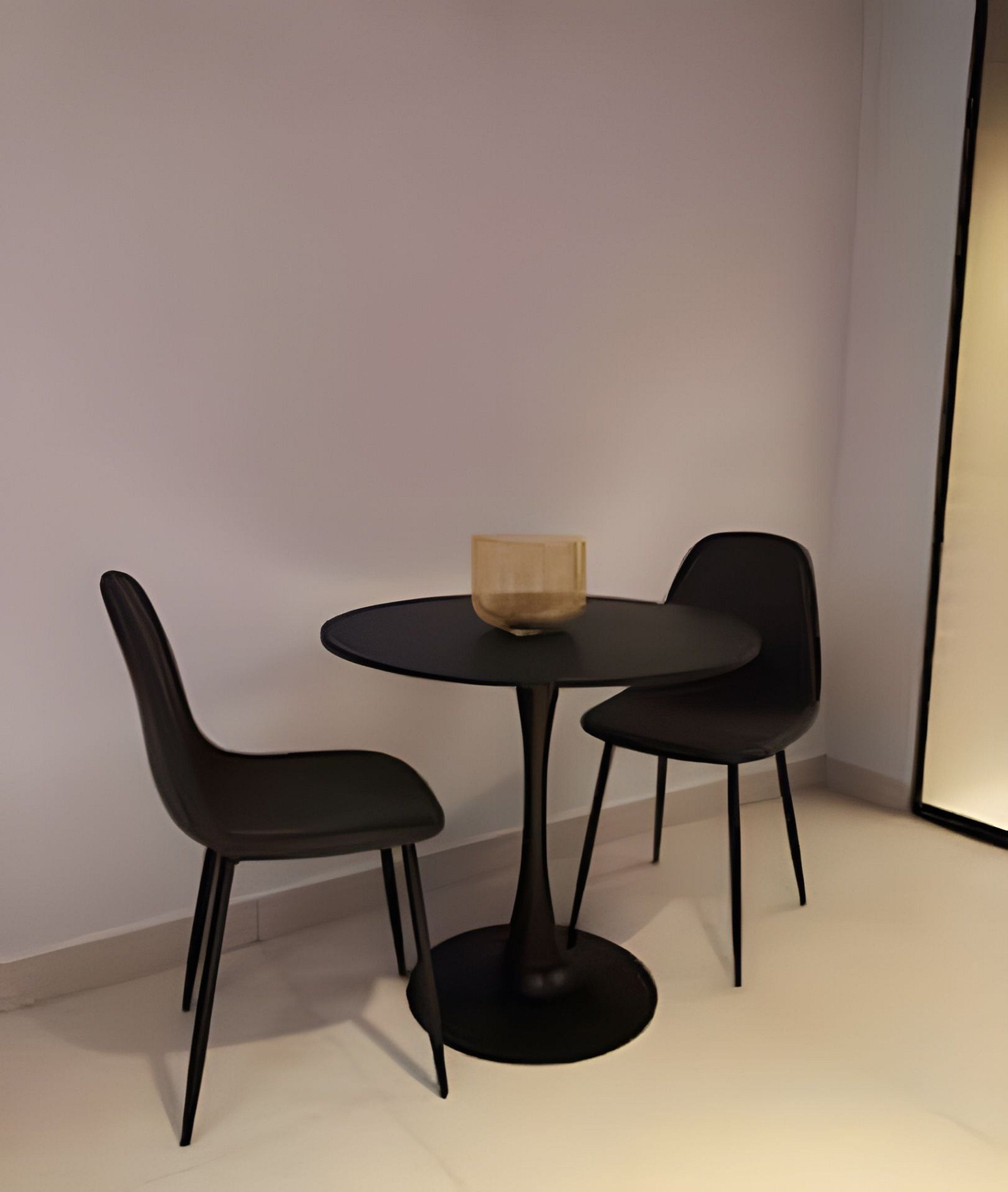 Una habitación pequeña y moderna con una mesa redonda y dos sillas negras.