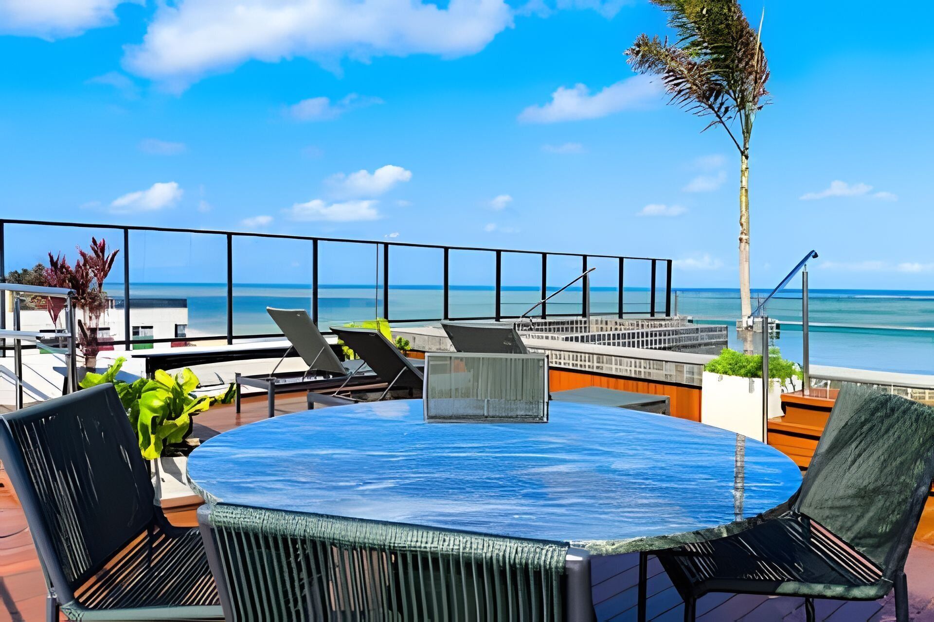 A round table with chairs on a deck overlooking a beach.