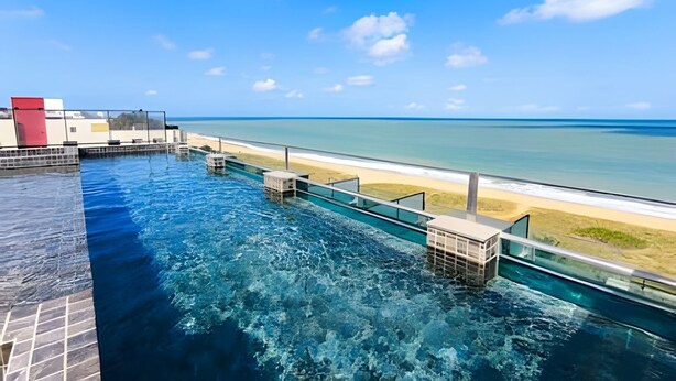 Una piscina azul cristalina con una barrera de vidrio, una estructura roja y vista a la playa.