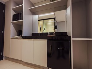 A modern kitchen with white cabinets, a black refrigerator, and a microwave on the countertop. - Alta Garden (João Pessoa)