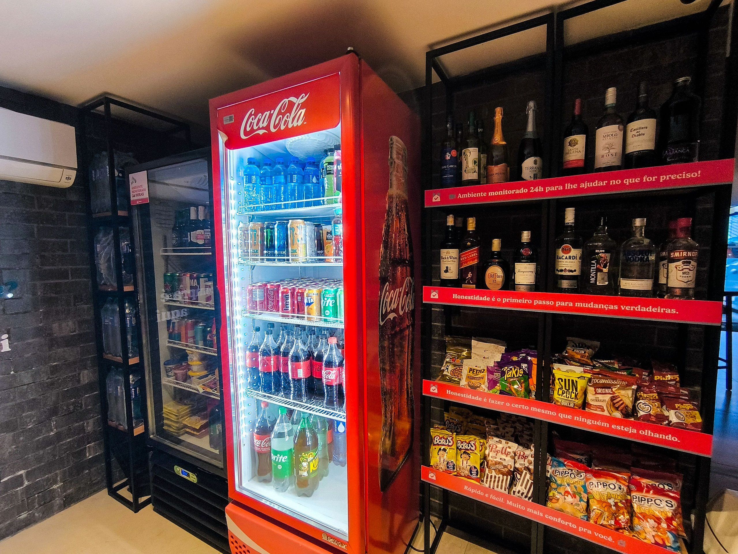 Un distributeur automatique proposant des Coca-Cola et diverses collations, ainsi qu’une étagère remplie de bouteilles d’alcool.