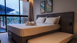 Habitación de hotel moderna con una cama grande, un banco y vistas a palmeras a través de la ventana.