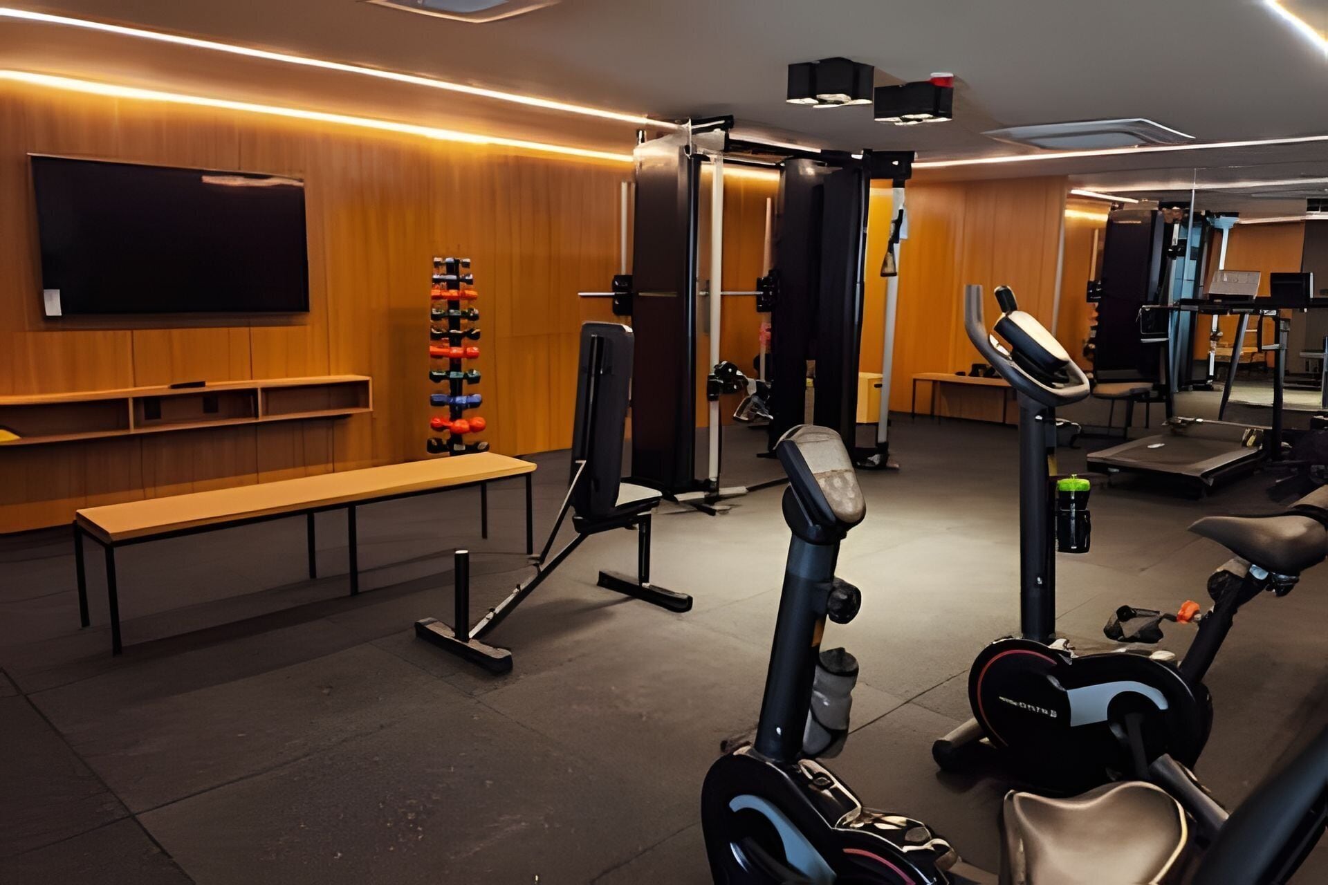 Un gimnasio con equipo de ejercicio, una banca y una televisión montada en la pared.