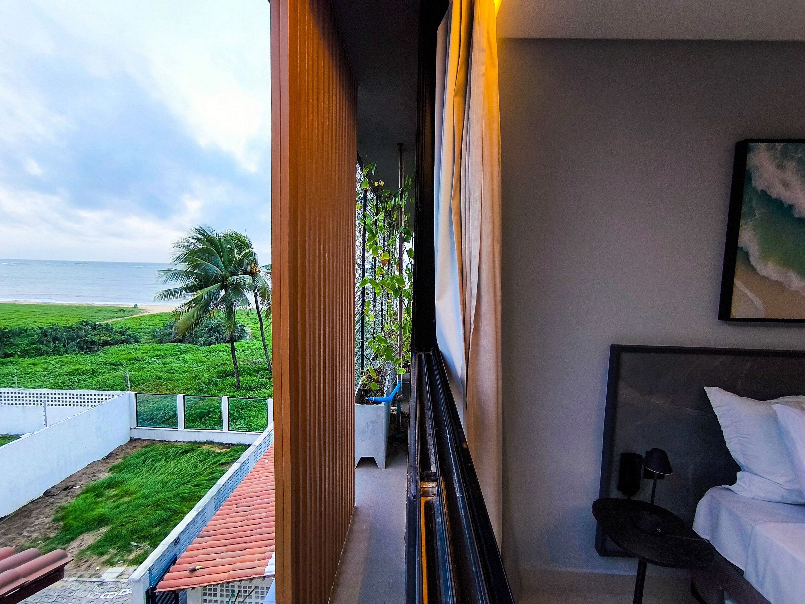 A hotel room with a balcony overlooking a beach and greenery.
