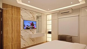 A modern bedroom with a large bed, a TV mounted on a marble wall, and built-in storage. - Westbrook Hotel & Offices (Owerri)