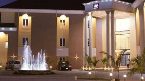 A hotel with a fountain in front, a covered entrance, and a sign with a crown logo. - Westbrook Hotel & Offices (Owerri)