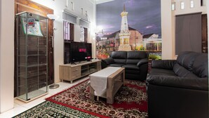 Ein Wohnzimmer mit einem großen Flachbildfernseher, einem schwarzen Ledersofa, einem Holztisch und einem roten Teppich mit Muster.