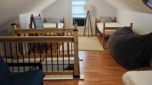 Une chambre mansardée chaleureuse, avec deux lits, un escalier en bois et une lucarne.