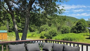 A wooden deck with a sectional sofa and a metal table. - Cozy 3-bedroom house minutes to Okemo and downtown Ludlow (Mount Holly)