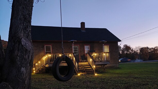 Un bâtiment en bois doté d’un porche, d’une balançoire faite d’un pneu et de guirlandes lumineuses.