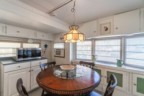 A kitchen with a round wooden table, white cabinetry, and a hanging light fixture. - Cozy, Perfect Conch Cottage! - VO315 (Summerland Key)