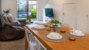 Una sala de estar moderna con una mesa de comedor preparada para cuatro personas, un sofá, un televisor y una puerta corrediza de vidrio a un jardín trasero.
