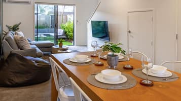 A modern living room with a dining table set for four, a sofa, a TV, and a sliding glass door to a backyard.