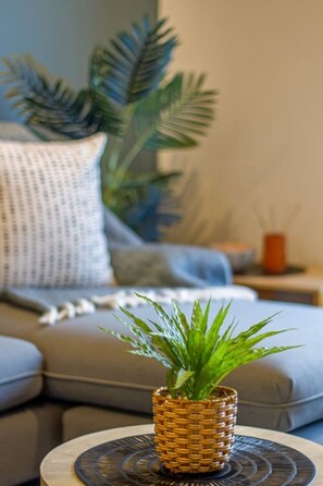 Een woonkamer met een bank, een klein rond tafeltje met een geweven plant, en een decoratief object op de bijzettafel.